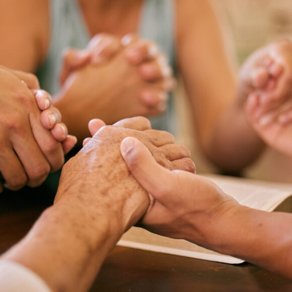 Shot of a group of people holding hands in prayer.