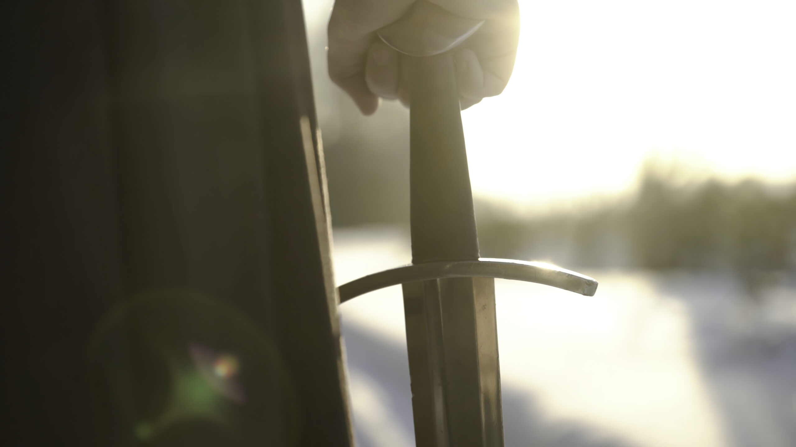 War and Peace Man in medieval suit holding sword. Action. Close-up of man's hand in medieval suit holding sword hilt on background of sunlight. Epic view of medieval hero