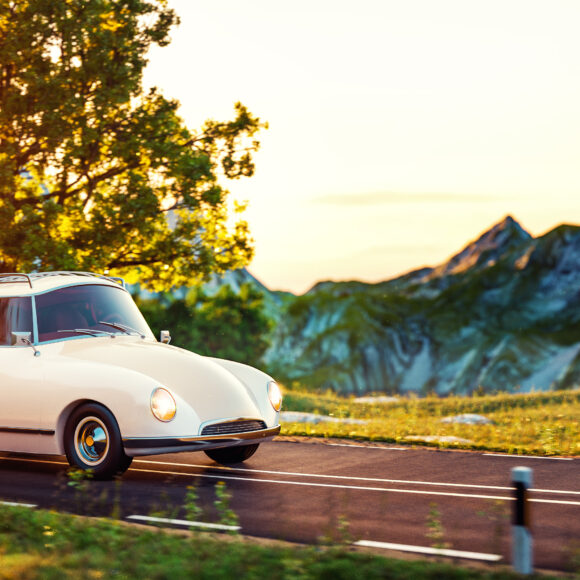 Cute little retro car goes by wonderful countryside road at sunset